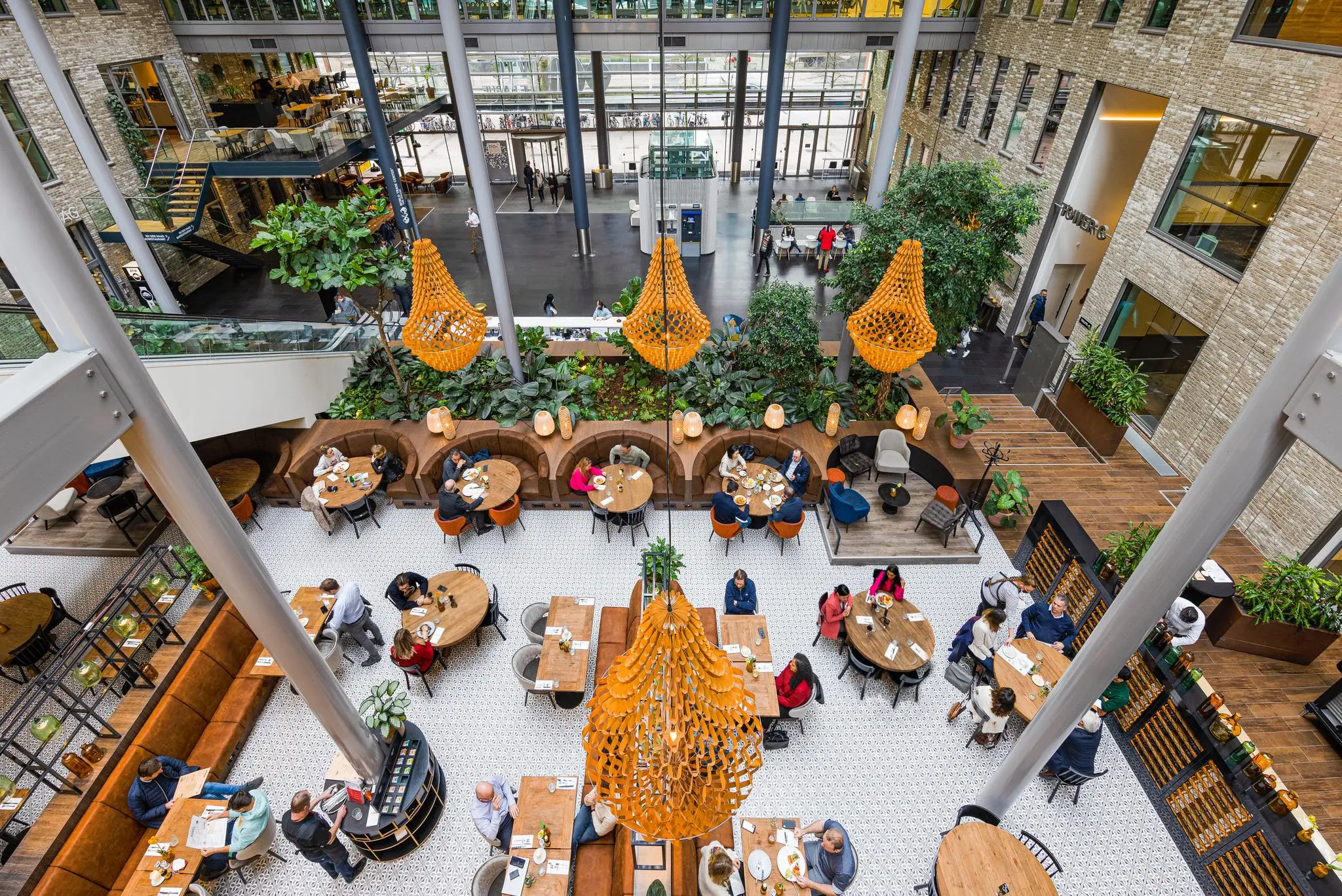 Overzicht van een moderne, drukbezochte binnentuin met zitgelegenheid in het gebouw aan de Prinses Beatrixlaan.